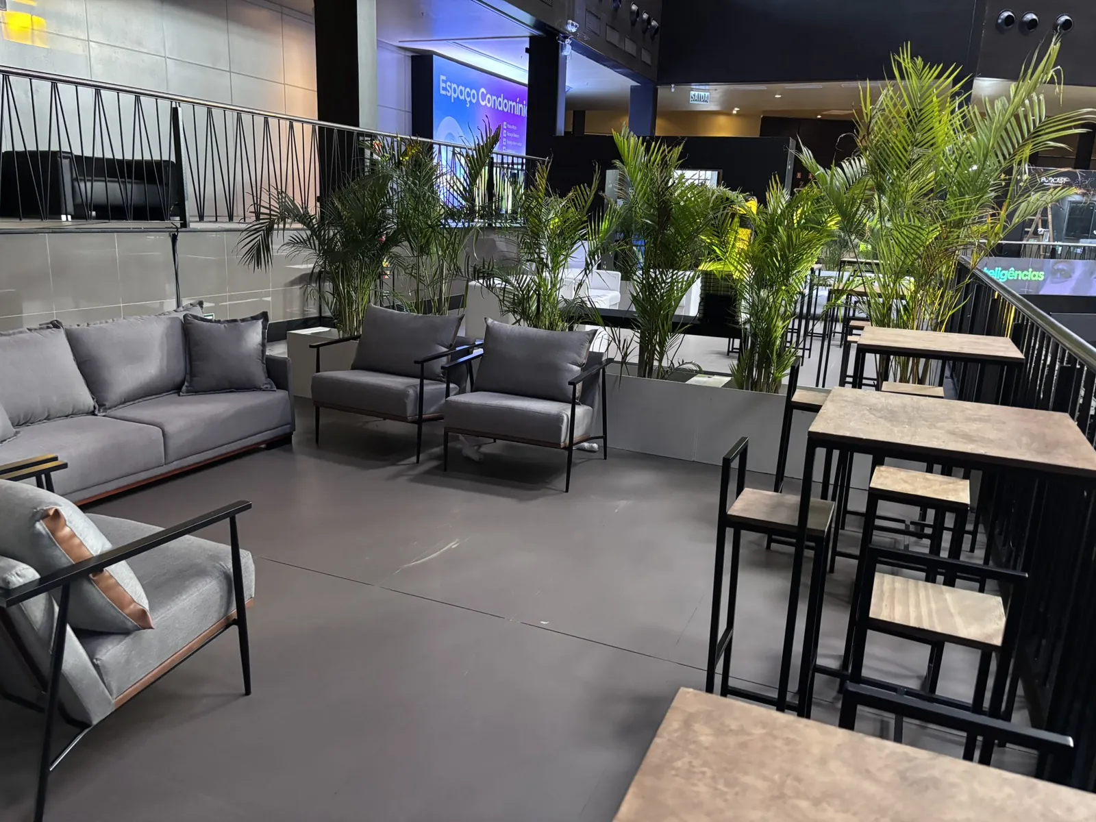 Lounge de evento com sofás, plantas e mesas altas